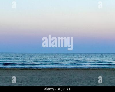 Picturesque beach landscape in Spain captured at dusk, featuring a soft pastel-colored sky, a calm and gently reflecting sea, and a quiet sandy beach. Stock Photo