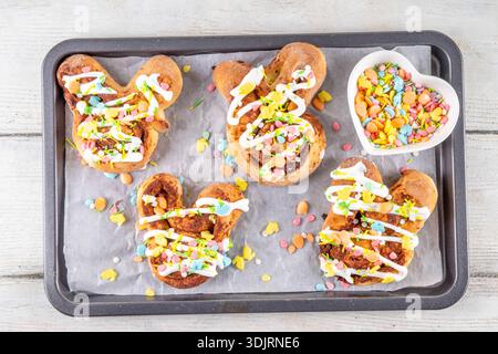 Cute and tasty Easter bunny cinnamon roll buns. Sweet bunny shaped buns, glazed and topped with colorful Easter sugar sprinkles, easter decorations, c Stock Photo