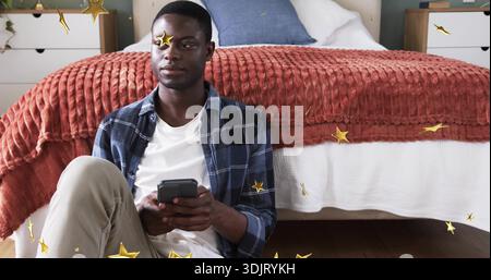 Sitting man using smartphone on wood floor by bed, rust throw, pillow, gold stars, copy space Stock Photo