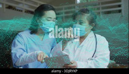 Reviewing tablet masked team in scrubs and labcoat pointing in clinic with teal overlay stethoscope Stock Photo