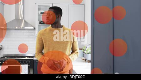 Standing man clasping hands at island in kitchen with range hood, mustard sweater, orange overlays Stock Photo