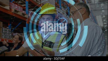 Scanning worker in yellow hard hat, hi-vis vest using handheld scanner in pallet racking aisle, HUD Stock Photo