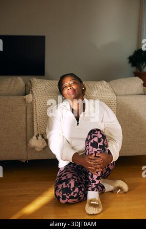 Mature woman sitting with eyes closed near sofa on floor at home Stock Photo