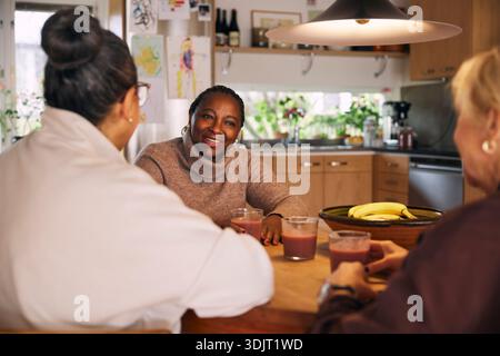 Smiling mature woman enjoying hot chocolate with friends at home Stock Photo