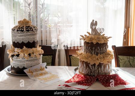 A beautifully crafted two-tier wedding cake adorned with intricate lace patterns, cream-colored flowers, and a couple silhouette topper, set on a tabl Stock Photo