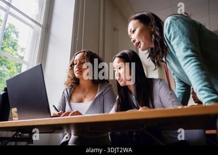 Low angle view of female teacher assisting students studying on laptop in classroom at university Stock Photo