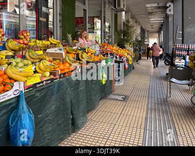 Athens fruit market stall beneath a pedestrian arcade. Fresh produce display with bananas, oranges, and apples in central Greece. Stock Photo