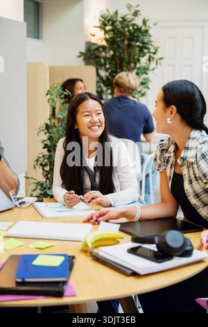 Smiling female young students talking with each other while sitting at table in college campus Stock Photo