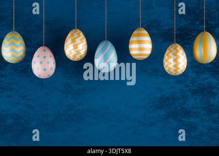 Hanging Easter eggs with various patterns in gold, pink, and blue on a textured blue backdrop. 3d rendering Stock Photo