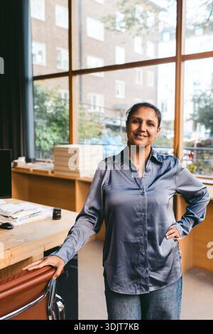 Smiling portrait of female design professional standing with hand on hip in office Stock Photo