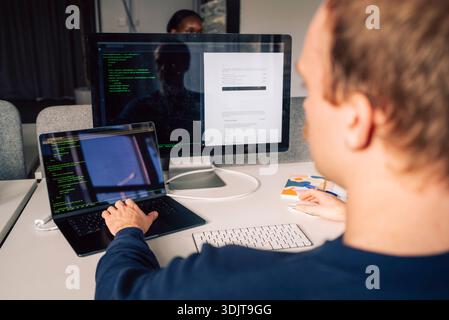 Rear view of male tech expert using laptop and computer in startup office Stock Photo