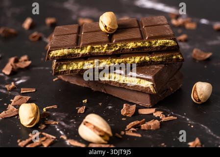 Stack of chocolate bars with pistachio filling on a dark background, surrounded by nuts and chocolate shavings, known as Dubai chocolate. Perfect for Stock Photo