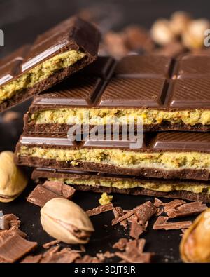 Stack of chocolate bars with pistachio filling on a dark background, surrounded by nuts and chocolate shavings, known as Dubai chocolate. Perfect for Stock Photo