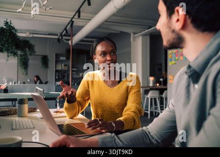 Female business expert discussing ideas with male colleague while working in tech startup office Stock Photo