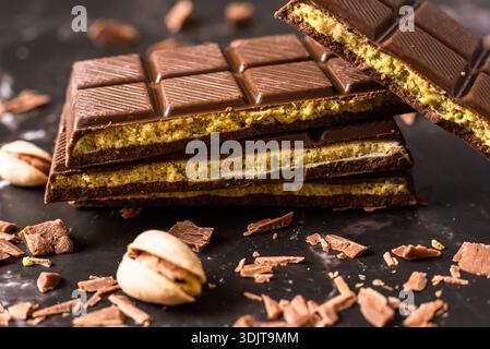Stack of chocolate bars with pistachio filling on a dark background, surrounded by nuts and chocolate shavings, known as Dubai chocolate. Perfect for Stock Photo