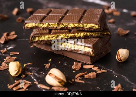 Stack of chocolate bars with pistachio filling on a dark background, surrounded by nuts and chocolate shavings, known as Dubai chocolate. Perfect for Stock Photo