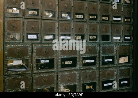 Rows of metal mailboxes are lined up in a building. Each box has a number and some have names. The scene is bright. Stock Photo