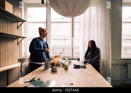 Male tech professional talking with female colleague while standing near table in startup office Stock Photo