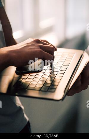 Hand of businessman holding smart phone while pressing key on laptop Stock Photo