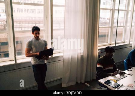 High angle view of young male business entrepreneur using laptop while standing near window in office Stock Photo