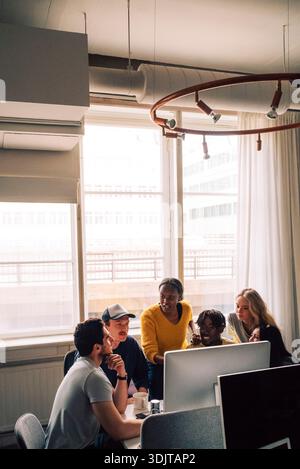 Female business professional discussing ideas with colleagues on desktop PC in startup office Stock Photo