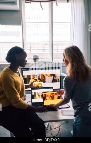 Female tech professionals discussing software design preview on different devices in office Stock Photo