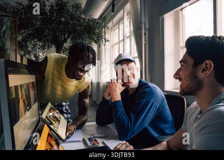 Smiling male creative tech professionals working on responsive design preview on with devices in office Stock Photo