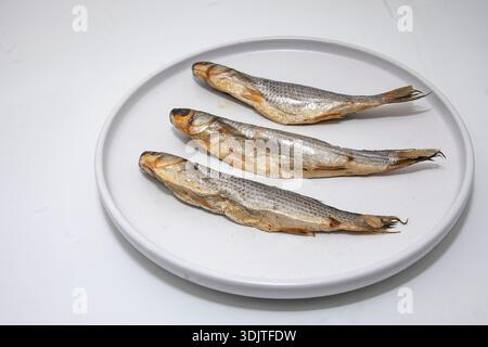 Dried whole fish arranged on white plate isolated on light background top view Stock Photo