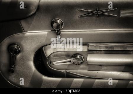A close‑up view of a vintage American car door panel showcases chrome window cranks, a classic door handle, and mid-century two‑tone upholstery Stock Photo