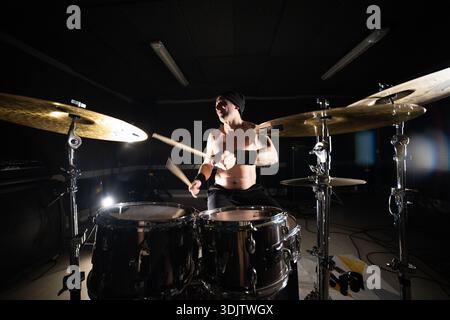 Energetic drummer performing live music in a dark studio Stock Photo