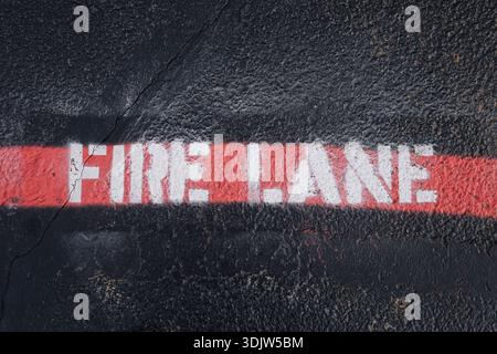 Fire lane road marking painted in red on asphalt surface. Emergency access zone with warning text on pavement. Urban traffic regulation public safety Stock Photo