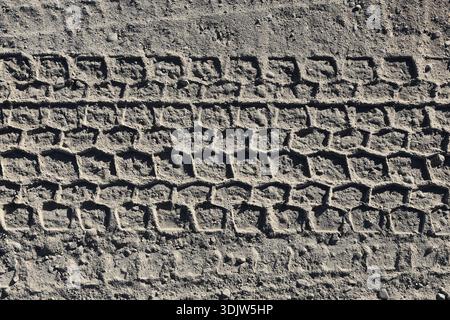 Vehicle tire tracks pressed into dry sand surface. Repeating pattern texture made by car wheels. Transportation trace background showing movement. Stock Photo