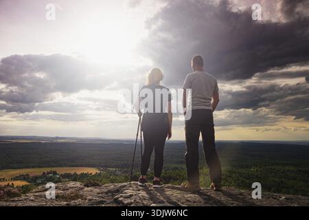 Couple man and woman tourist at top of mountain in shirt and black trousers hiking at mountain peak above clouds Stock Photo
