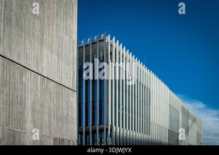 A modern architectural building featuring clean lines, vertical metal fins, and a contrasting concrete façade, set against a clear blue sky. Stock Photo