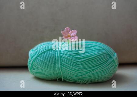 Mint green yarn ball with handmade pink glass flower pin on soft neutral background Stock Photo