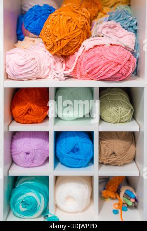 Multicolored yarn balls organized in white shelving unit for knitting and crochet storage Stock Photo