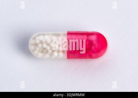 closeup single pink white capsule resting on textured white surface, clear halfshell reveals tiny beads, studio lighting highlights glossy finish, ide Stock Photo