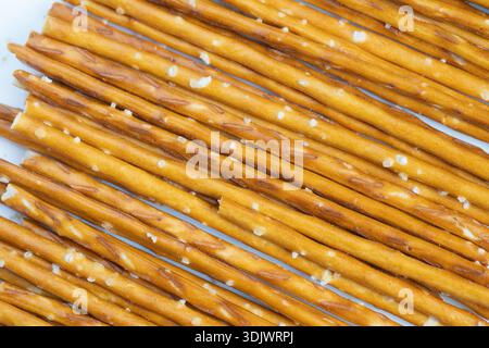 Golden pretzel sticks with coarse salt, arranged in tight rows on neutral background, crunchy surface with visible salt crystals, warm brown tones, id Stock Photo
