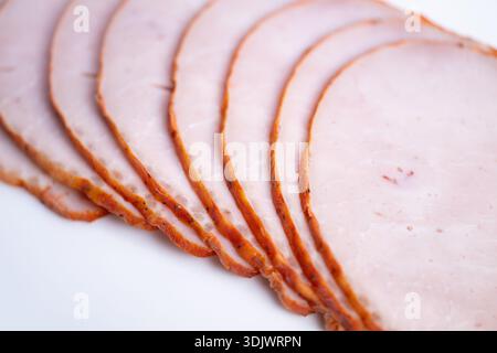 thin sliced ham on white background, arranged in neat overlapping rows with glossy edges and visible grain, closeup texture emphasizes pink center and Stock Photo