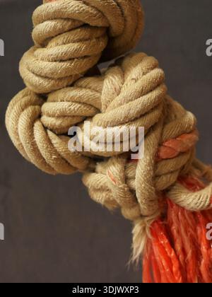 Knotted climbing rope with a rough surface and frayed orange ends against a dark background in a sports hall. Close-up. Space for text. Stock Photo