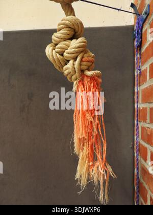Knotted climbing rope with a rough surface and frayed orange ends against a dark background in a sports hall. Close-up. Space for text. Stock Photo