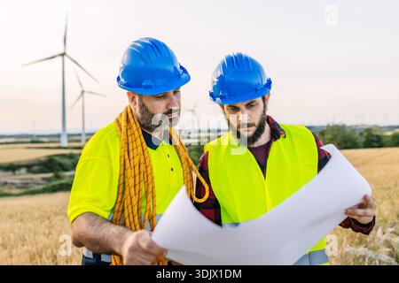 Engineers discussing wind turbine project blueprint on site Stock Photo