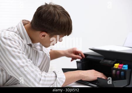Man checking printer ink levels at white desk in office Stock Photo