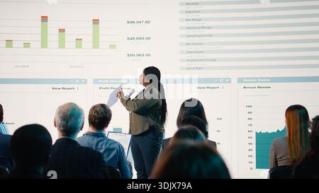 African american woman makes a speech at international summit in conference hall, presentation with reports and investments for networking. Speaker engages audience in business forum. Stock Photo
