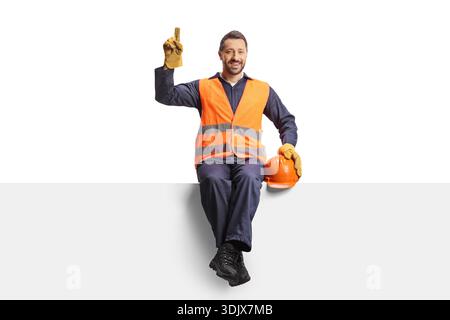 Happy construction worker sitting on a blank panel and pointing up isolated on white background Stock Photo