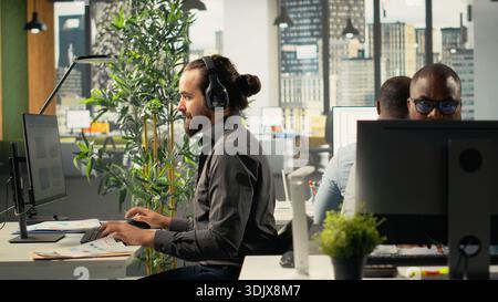 Business people gathered around laptops working on project tasks and targets for development. Office environment promotes synergy, teamwork and insight through analytics and planning. Stock Photo