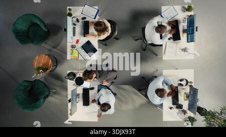 Top down view of employees team discuss business intel and performance in office. Multinational company staff members reviews reports, forecasts and diagrams to align strategy. Stock Photo