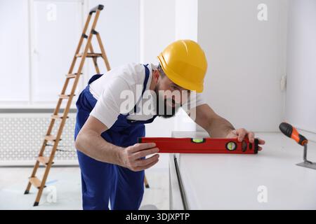Worker measuring white dresser with building level indoors Stock Photo