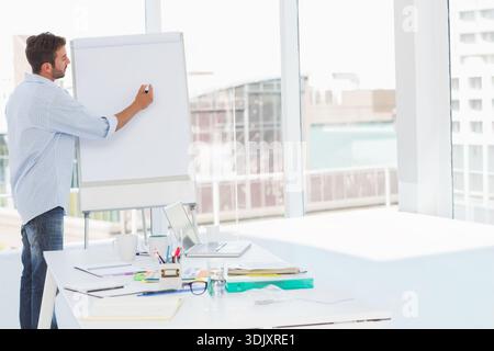 Flip chart is being written on near floor-to-ceiling windows in office, laptop, supplies on table. Presenter, brainstorming, collaboration, modern, br Stock Photo