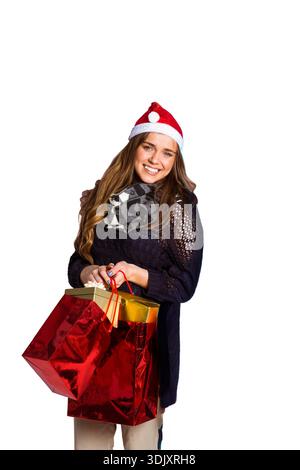 Woman smiling, wearing red Santa hat, patterned scarf, holding red bags and gold box in studio. Festive, gifts, holiday, portrait, cheerful, gold, bac Stock Photo